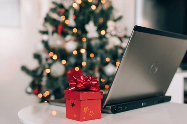 istock Small red present with gift bow next to laptop on table in front of decorated christmas tree 1462969231