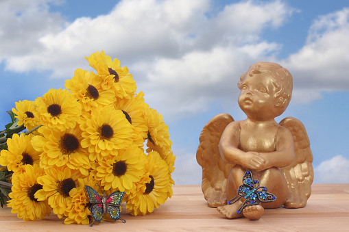 Yellow flowers and angel statue with butterflies on blue sky background