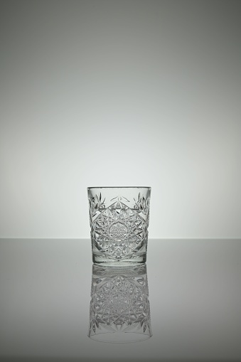 A crystal water glass reflecting on a gray surface with white background