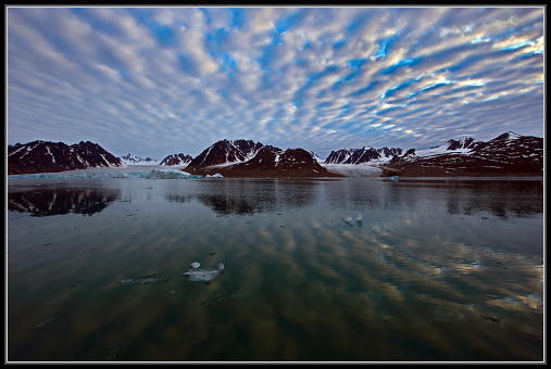 The still waters of the ocean surrounding Svalbard, Norway under beautiful altocumulus clouds