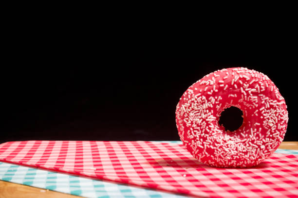 A closeup of a glazed fresh donut on chequered tablecloths on a cutting board