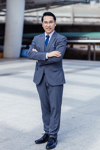 Asian Mature businessman with arms crossed smiling happy at the city Confident rich business man executive standing looking at camera business success Leadership concept Confident man in suit