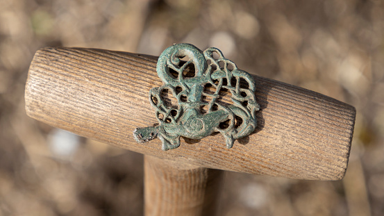 An Iron Age fibula, intact, bronze, placed on a spade handle