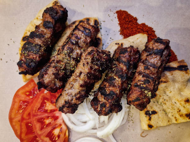 istock Grilled minced meat called soutzoukakia prepared and served with Greek pie bread, sliced onions, and tomatoes top view close up. 1462976890