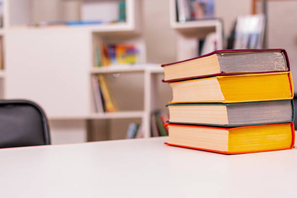 istock Thick old books with colorful covers lie in pile on white office table against backdrop of bookshelf 1462977565