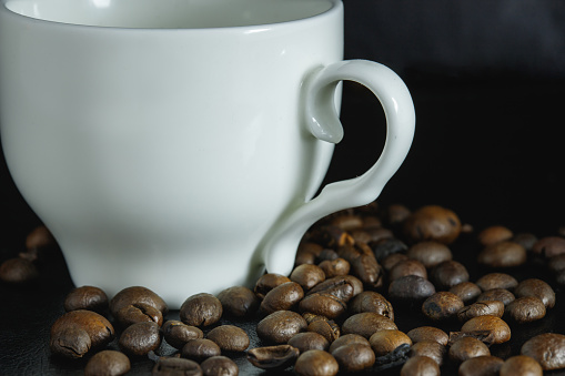 A close-up shot of a white coffee cup surrounded by coffee beans isolated on a blurry background