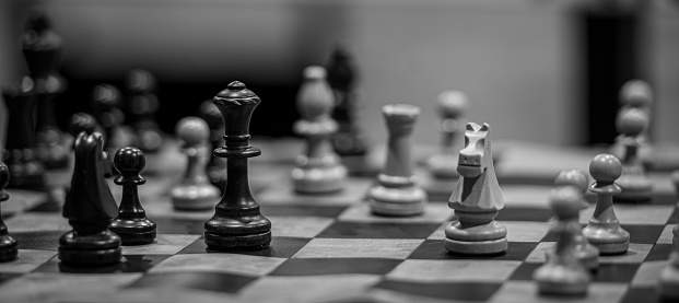 The close-up grayscale shot of a chess board with wooden figures
