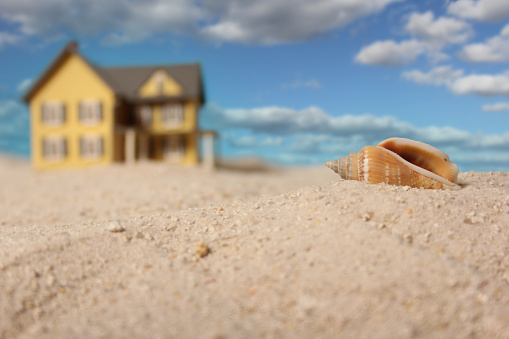 A seashell in the background of a toy house on the beach.