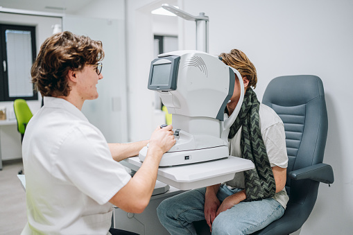 Ophthalmologist examining patient's eyes. Side view of White man is checking the eye vision with phoropter eyesight measurement testing machine. Medical check up. Handsome man getting an eye exam at ophthalmology clinic. Checking retina of a male eye close-up.