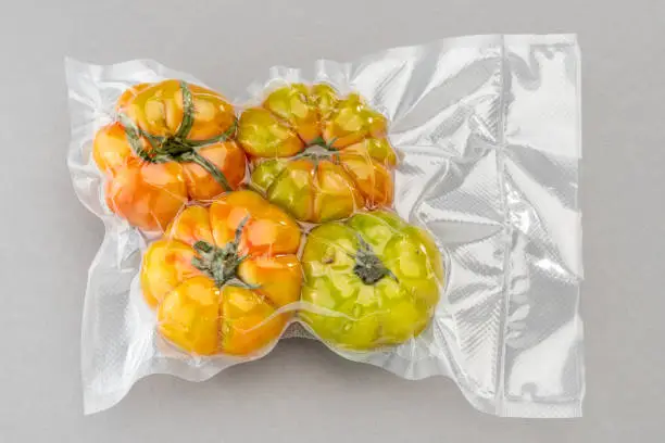 Green tomatoes in vacuum pack for sous vide cooking on gray background