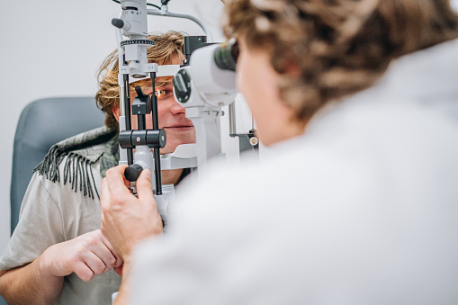 Ophthalmologist examining patient's eyes. Side view of White man is checking the eye vision with phoropter eyesight measurement testing machine. Medical check up. Handsome man getting an eye exam at ophthalmology clinic. Checking retina of a male eye close-up.