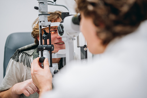 Ophthalmologist examining patient's eyes. Side view of White man is checking the eye vision with phoropter eyesight measurement testing machine. Medical check up. Handsome man getting an eye exam at ophthalmology clinic. Checking retina of a male eye close-up.