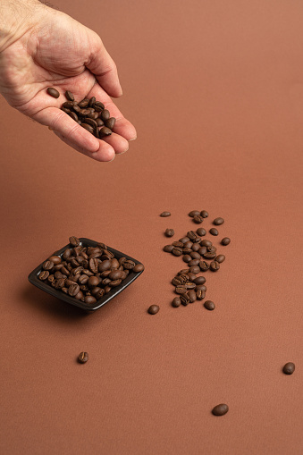 A vertical shot of a black bowl filled with coffee beans on the pink background