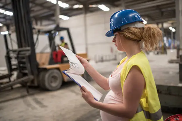 Photo of Pregnant worker woman in concrete factory looking note, looking at the work planning plan. Preparing labor