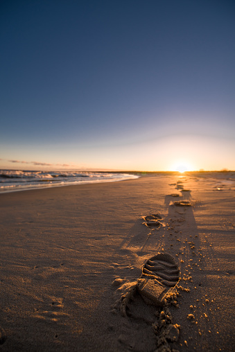 A vertical shot of the footprints on the sandy beach lit by sunlight at the sunset