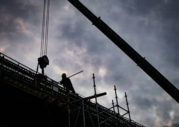 istock Silhouette of a worker and a crane on a construction site on cloudy sky background 1462996481