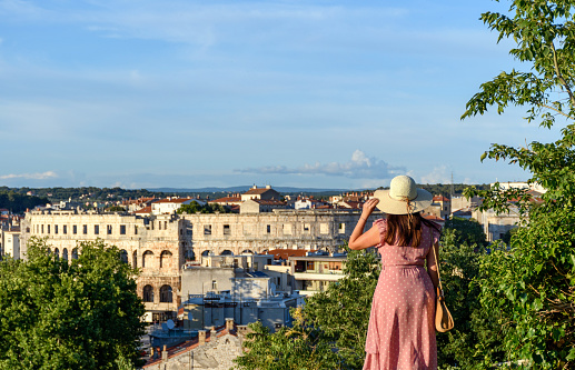 A woman wearing a long pink dress with a sun hat and looking at the scenery of Pula, Croatia