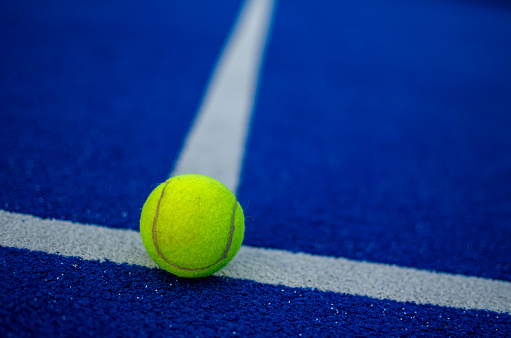 selective focus of a ball on the white line of a blue paddle tennis court. Sports concept