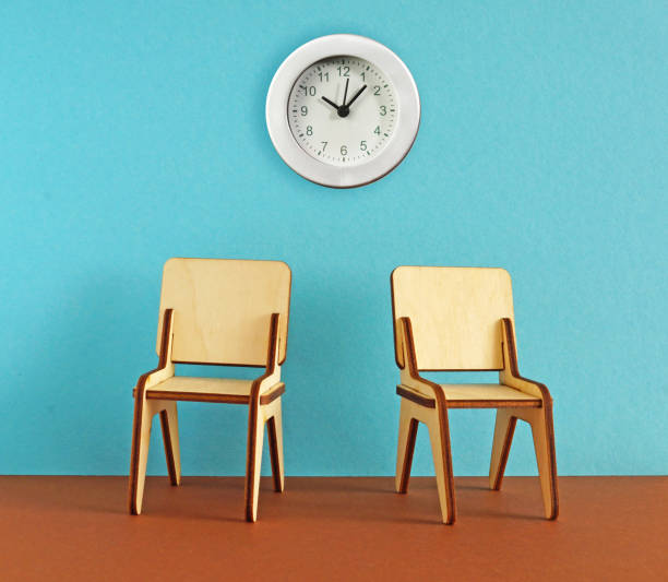 istock Waiting room with empty wooden chairs and wall clock. Two stools in the room 1463007337