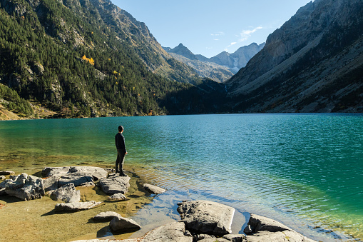 A young man traveler steps on rocks on the shore of Lac de Gaube in French Pyrenees