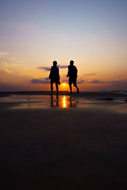 istock Silhouette of two people walking on wet sand during sunset 1463007920