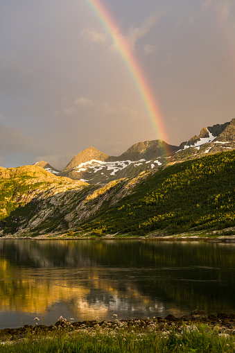 Rainbow over snowcapped mountains with midnight sun and norwegian fjord in the foreground