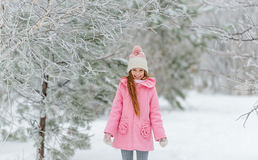 Cute girl in adorable pink coat smiling happily, enjoying being outside in winter