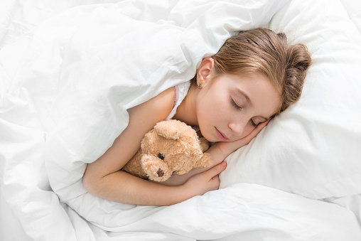 Amazing child napping and hugging her teddy bear in sleep, calm and peaceful