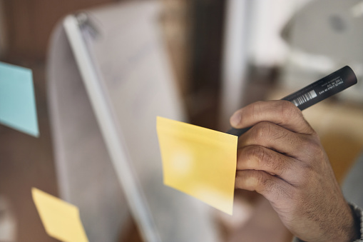 Photo of unrecognizable person writing on a transparent wipe board and thinking of a solution for his work-related problems.