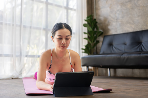 Healthy asian woman watching exercise clip on tablet Woman doing yoga at home to stay healthy and strong with online exercise on tablet at home in morning concept of relaxation and meditation