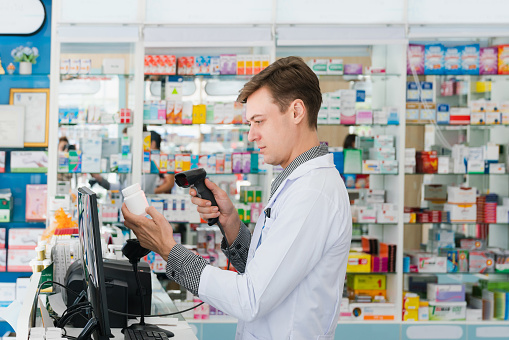 Portrait of a young pharmacist scanning the barcode of a mockup qualified pharmaceutical, medicine pill container or bottle for copyspace at pharmacy.