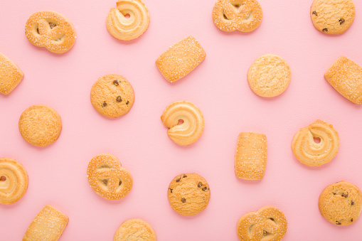 Different dry butter cookies on light pink table background. Pastel color. Closeup. Sweet snacks. Biscuit pattern. Top down view.