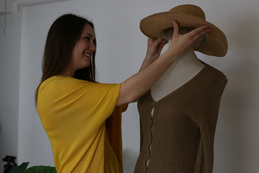 Young beautiful smiling woman works in her own boutique and  putting on the mannequin the clothes in warm tones