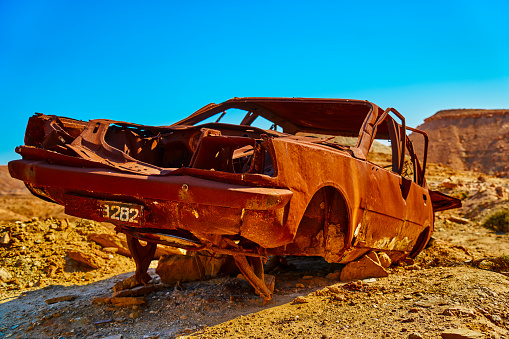 Completely rusted wrecked car in the desert hills of Tunisia under a blue sky
