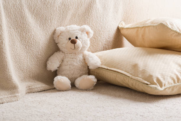 istock Smiling white teddy bear sitting on carpet at sofa and pillows at nursery room. Closeup. Front view. 1463063733