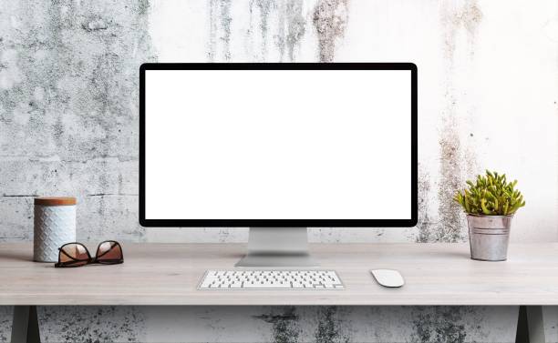 Computer display on office desk with isolated screen for mockup, wep page presentation. Clean desk with plant, glasses and box. White rough wall in the background