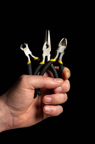 黒い背景に斜めのペンチとはさみツールを持つ男性の手の接写。電気の修理によく使用されます - pliers hand tool human hand work tool ストックフォトと画像