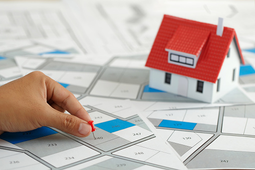 Hand holding red pin pointing to cadastral map to decide to buy land. real estate concept with vacant land for building construction and housing subdivision for sale, rent, buy, investment