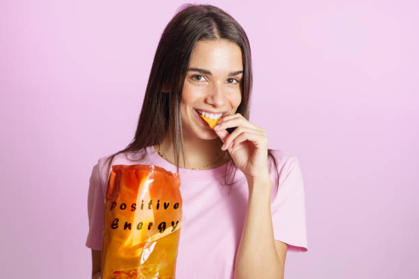 Woman eating tasty crisps pink background stock photo