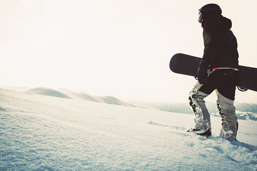 Snowboarder dressed in a full protective gear for extreme freeride snowboarding posing with a snowboard walking. Isolated on gray white snow background.