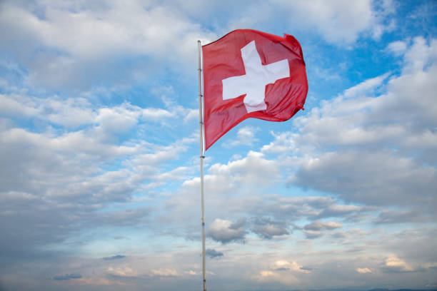 flag of Switzerland fluttering in the blue sky with cumulus clouds