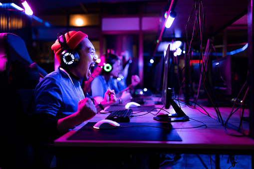 Cheerful Chinese man screaming of joy after winning in eSports video games at entertainment club.