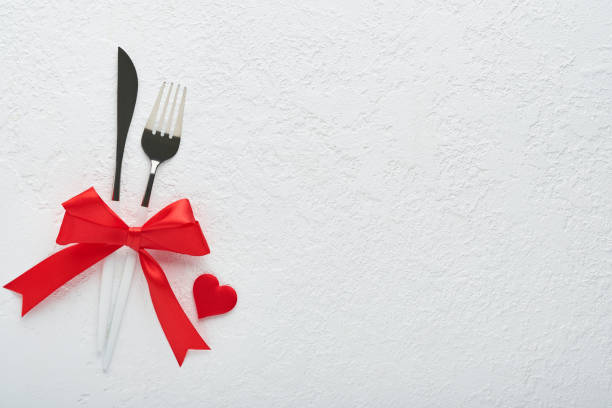 istock Valentines day romantic table setting. Empty or closeup of a dinner black plate, knife, fork and decorative silk hearts on white background. Holiday concept. Copy space for inscriptions. 1463098439