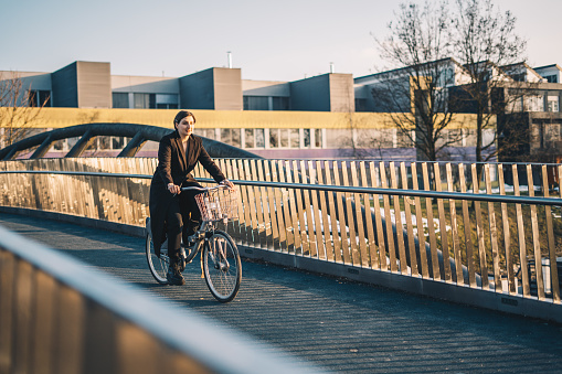 Woman cycling over a bridge stock photo. Woman riding towards the camera to her job during morning sun