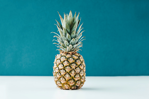 Single pineapple on a white table in front of blue colored wall.