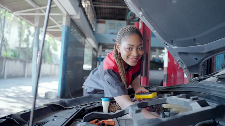 Portrait of an black mechanic woman in an automobile service and repair shop, smiling proudly as she checks an inspection list on engine room of a car.