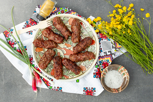 traditional meat rolls, called mititei on a   ceramic plate, with a bouquet of buttercup flowers