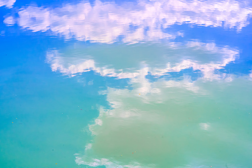 the blue sky and white clouds reflected on the water The ripples on the water's surface add a unique texture and artistic effect to the image.