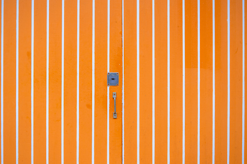 Orange door with white stripes. the metallic lock and handle on the door. The stripes on the door create a visually striking pattern.