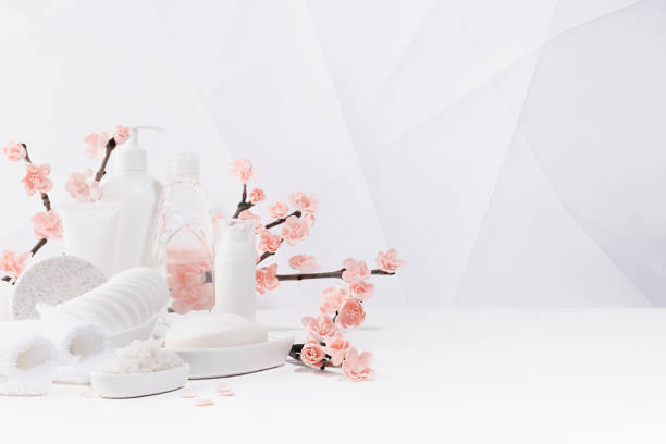 バス用の化粧品と美容製品、白いボトルのスパ、春のピンクの桜の花の枝、幾何学的なシンプルな都会的なスタイルの柔らかい明るい白いバスルームのテーブルの上のトイレタリー、コピー�